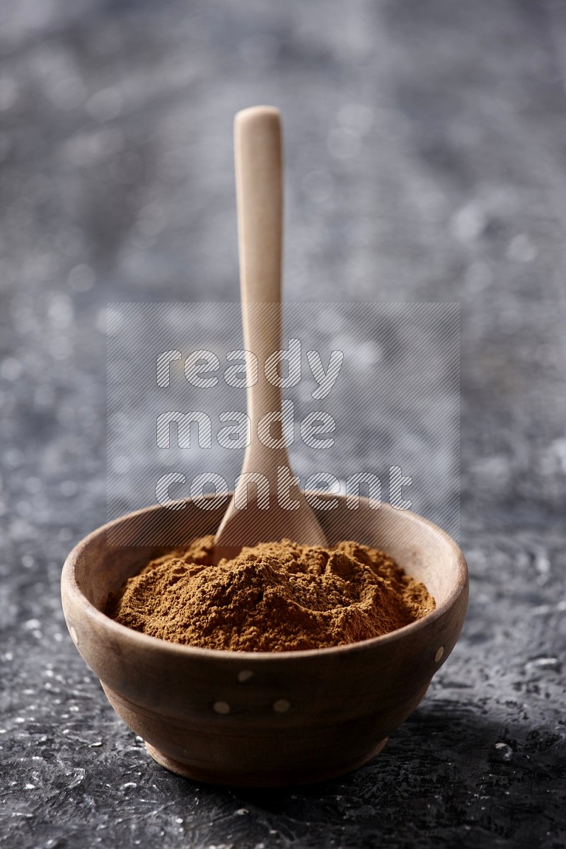 Wooden bowl full of cinnamon powder with a wooden spoon on a textured black background in different angles