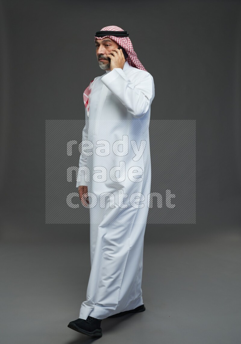Saudi man with shomag Standing talking on phone on gray background