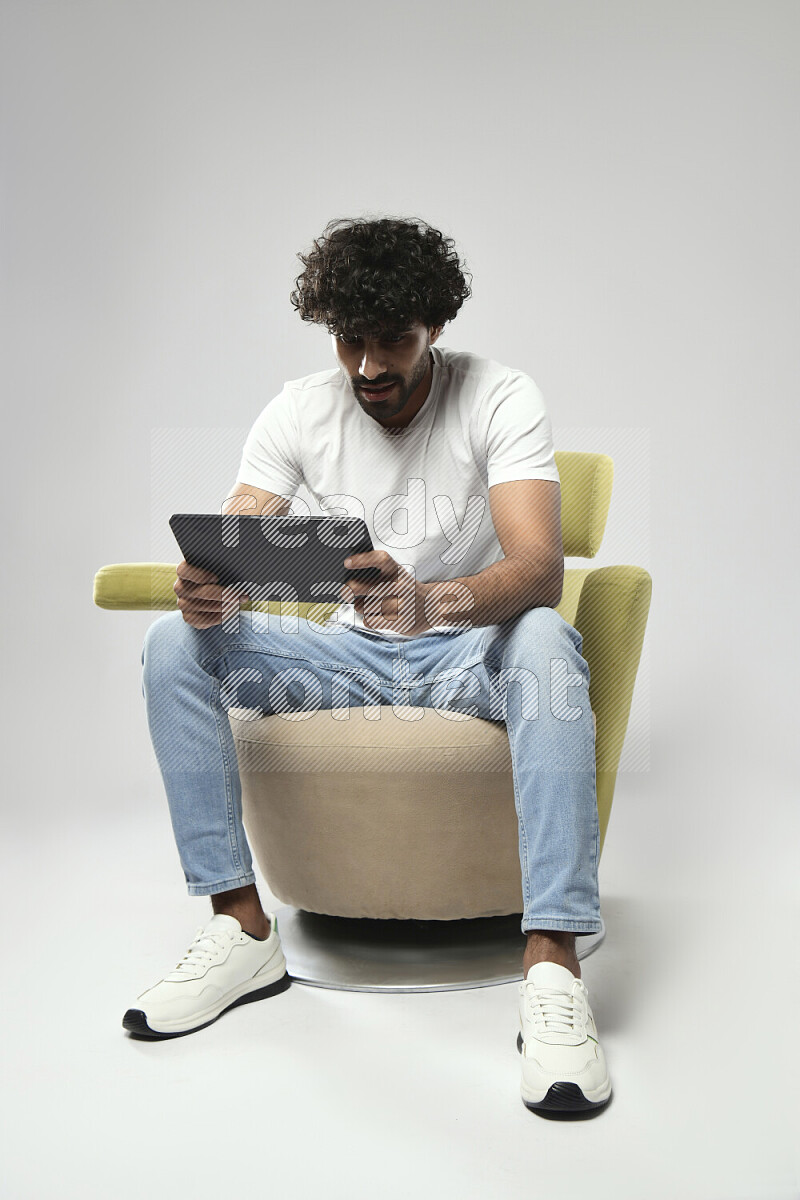 A man wearing casual sitting on a chair gaming on a tablet on white background