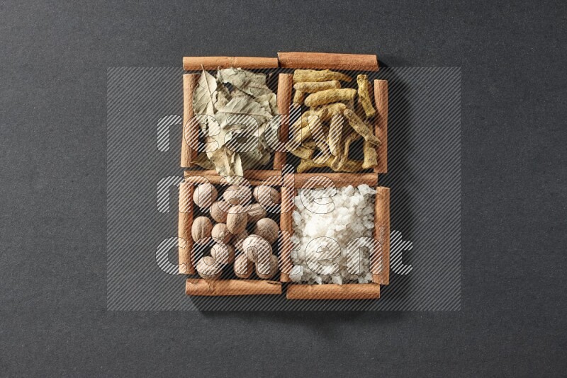 4 squares of cinnamon sticks full of bay laurel leaves, white salt, turmeric fingers and nutmegs on black flooring