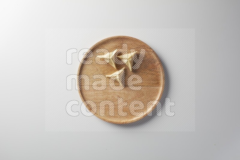 Three Sambosas on a wooden round plate on a white background