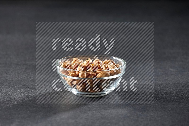 A glass bowl full of cashews on a black background in different angles