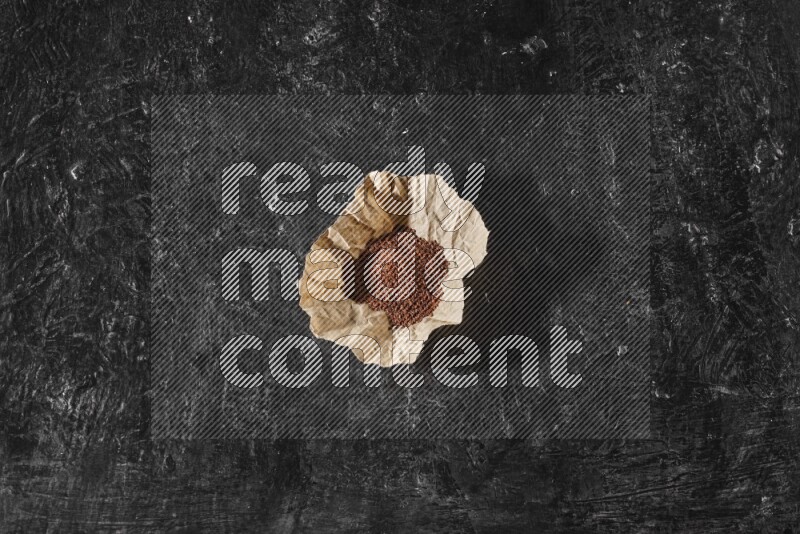 A crumpled piece of paper full of garden cress seeds on a textured black flooring