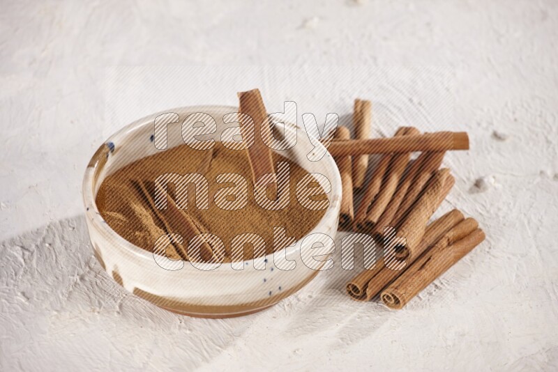 Ceramic bowl full of cinnamon powder with cinnamon sticks on the side on white background