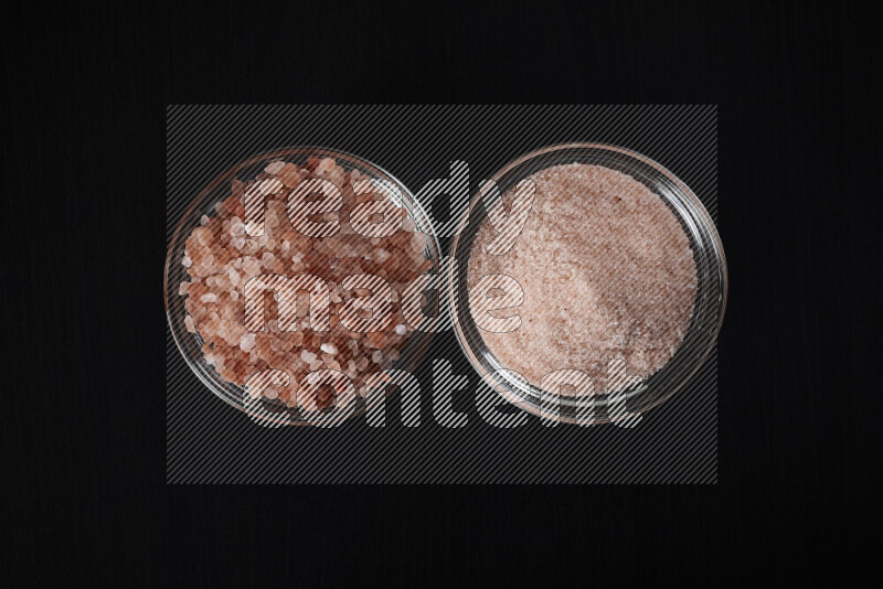 2 glass bowls one is filled with fine himalayan salt and the other with coarse himalayan salt on black background