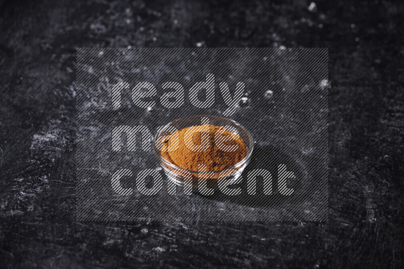 A glass bowl full of ground paprika powder on black background