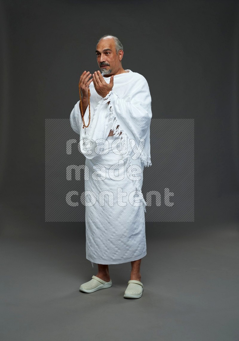 A man wearing Ehram Standing dua'a on gray background