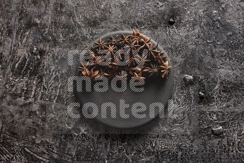 Star anise on a black plate on textured black background