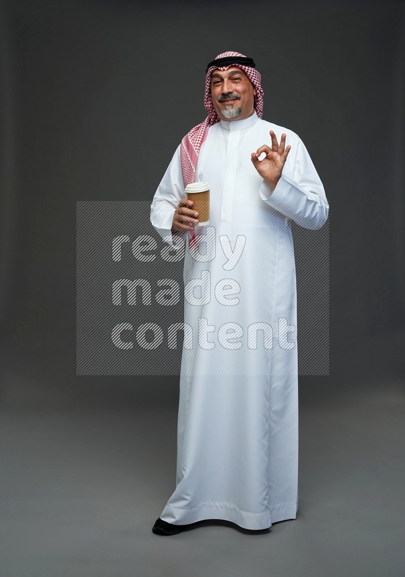Saudi man with shomag Standing holding paper cup on gray background