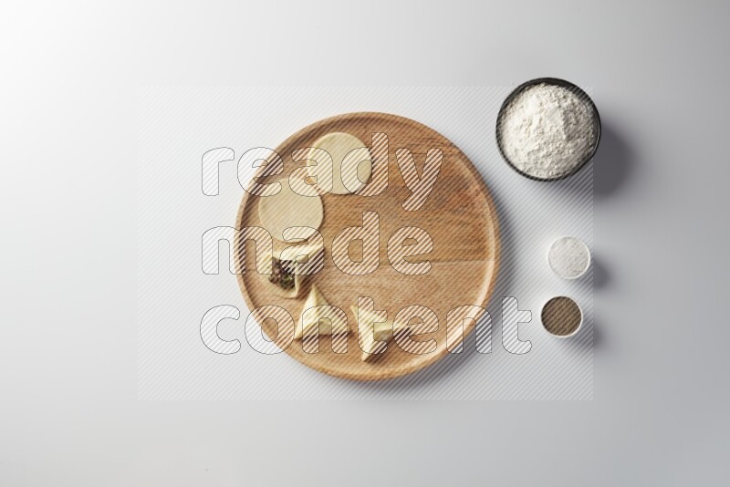 two closed sambosas and one open sambosa filled with meat while flour, salt, and black pepper aside in a wooden dish on a white background