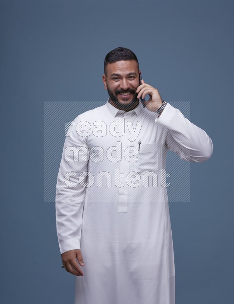 A Saudi man calling on blue background wearing Saudi Thob