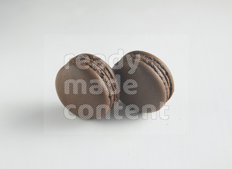 45º Shot of two Brown Dark Chocolate macarons on white background