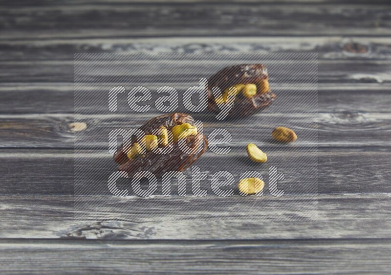 two pistachio stuffed madjoul dates on a wooden grey background
