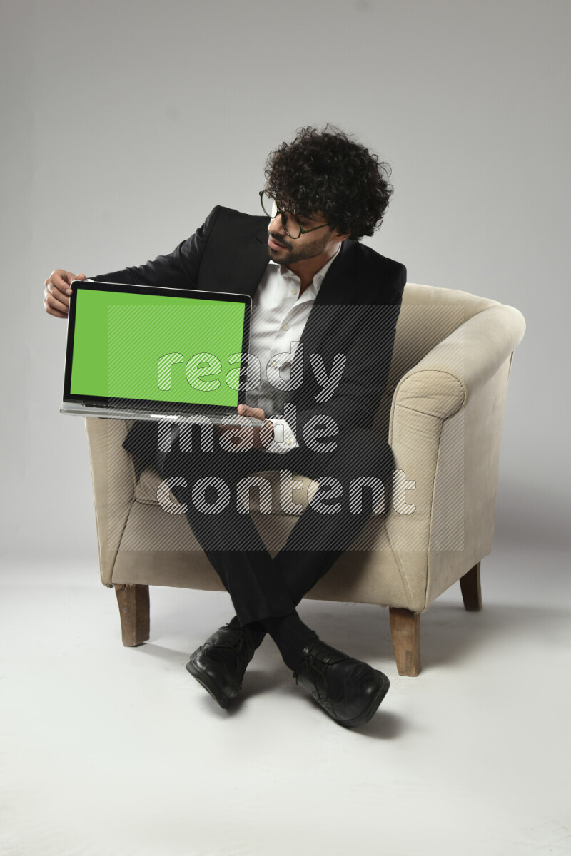 A man wearing formal sitting on a chair showing a laptop screen on white background