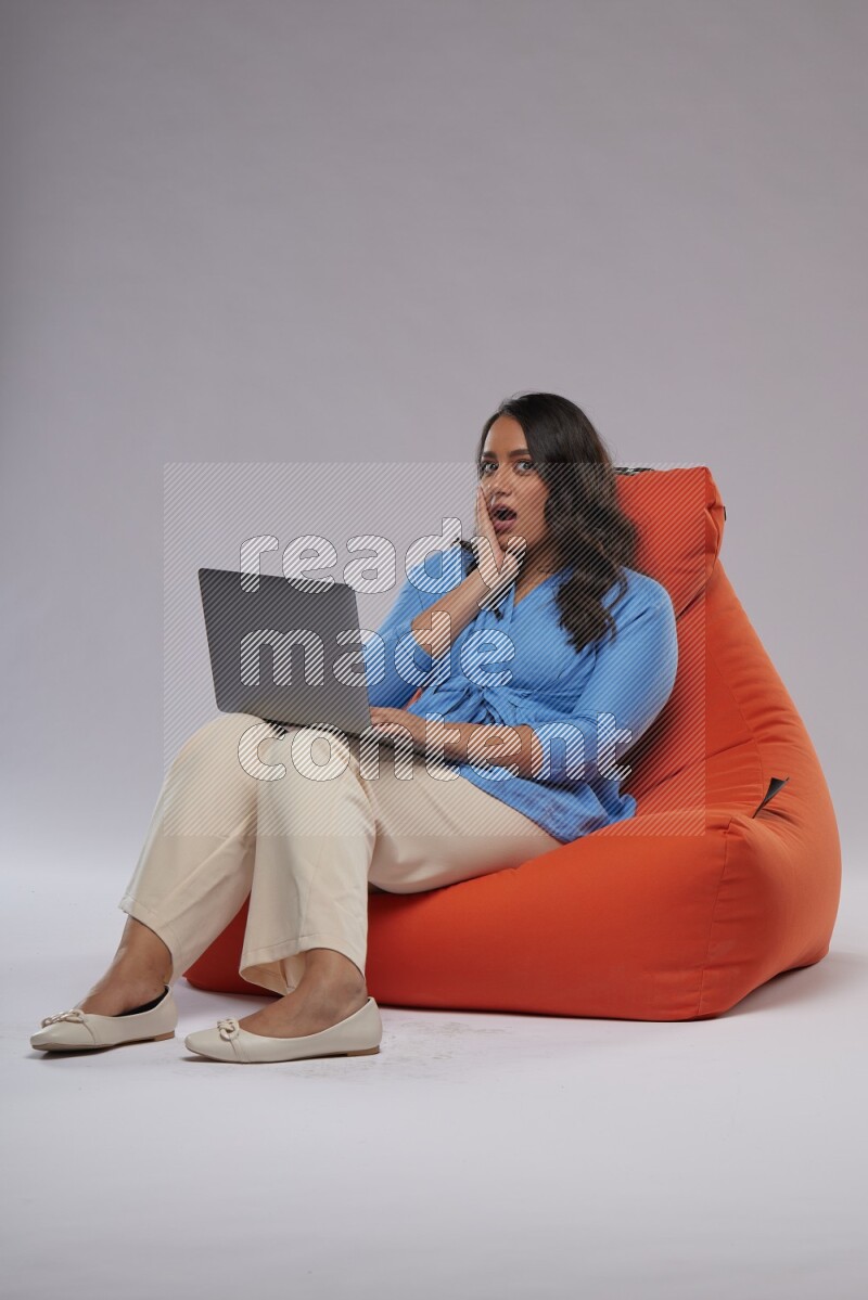 A woman sitting on an orange beanbag and working on laptop