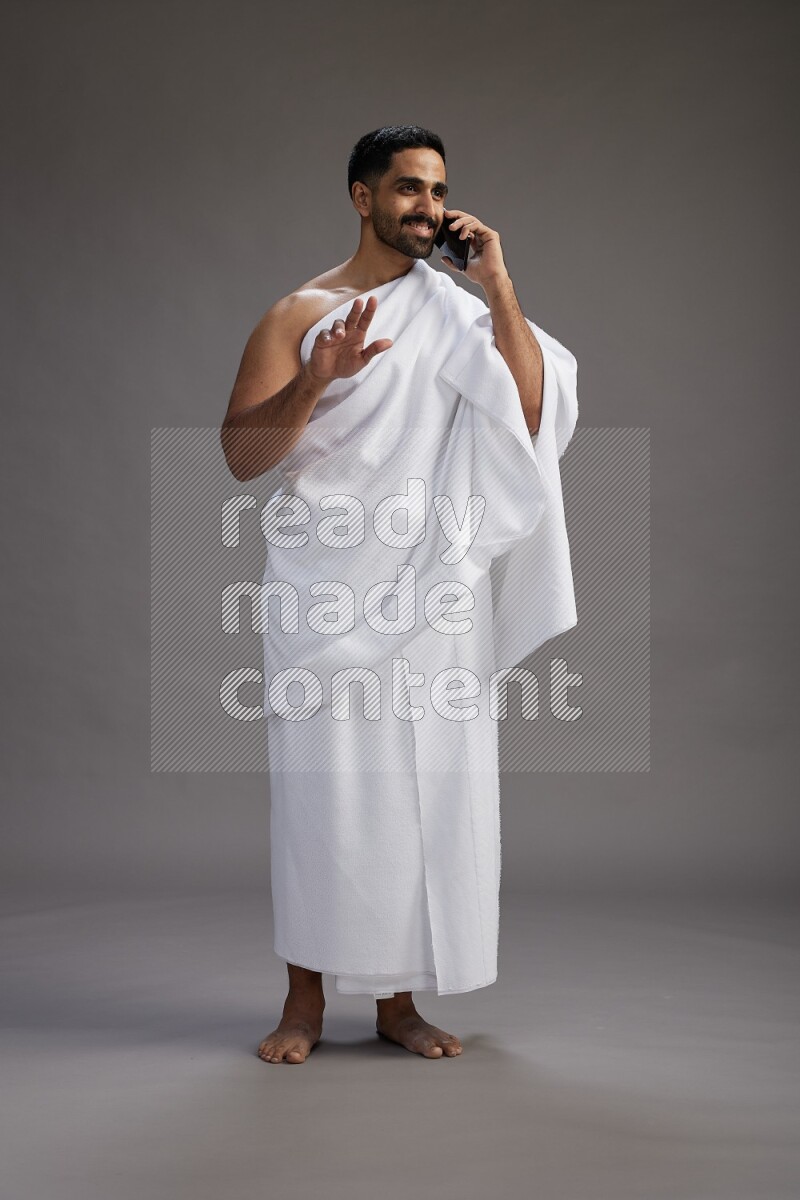 A man wearing Ehram Standing talking on phone on gray background