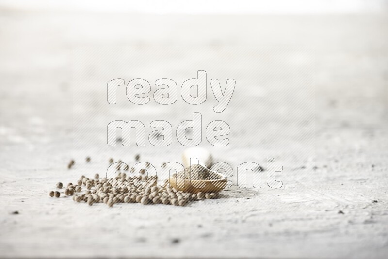 A wooden spoon full of white pepper powder and white pepper beads on textured white flooring
