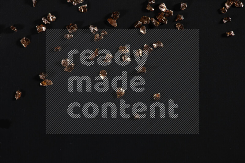 Bronze shimmering fragments of glass scattered on a black background