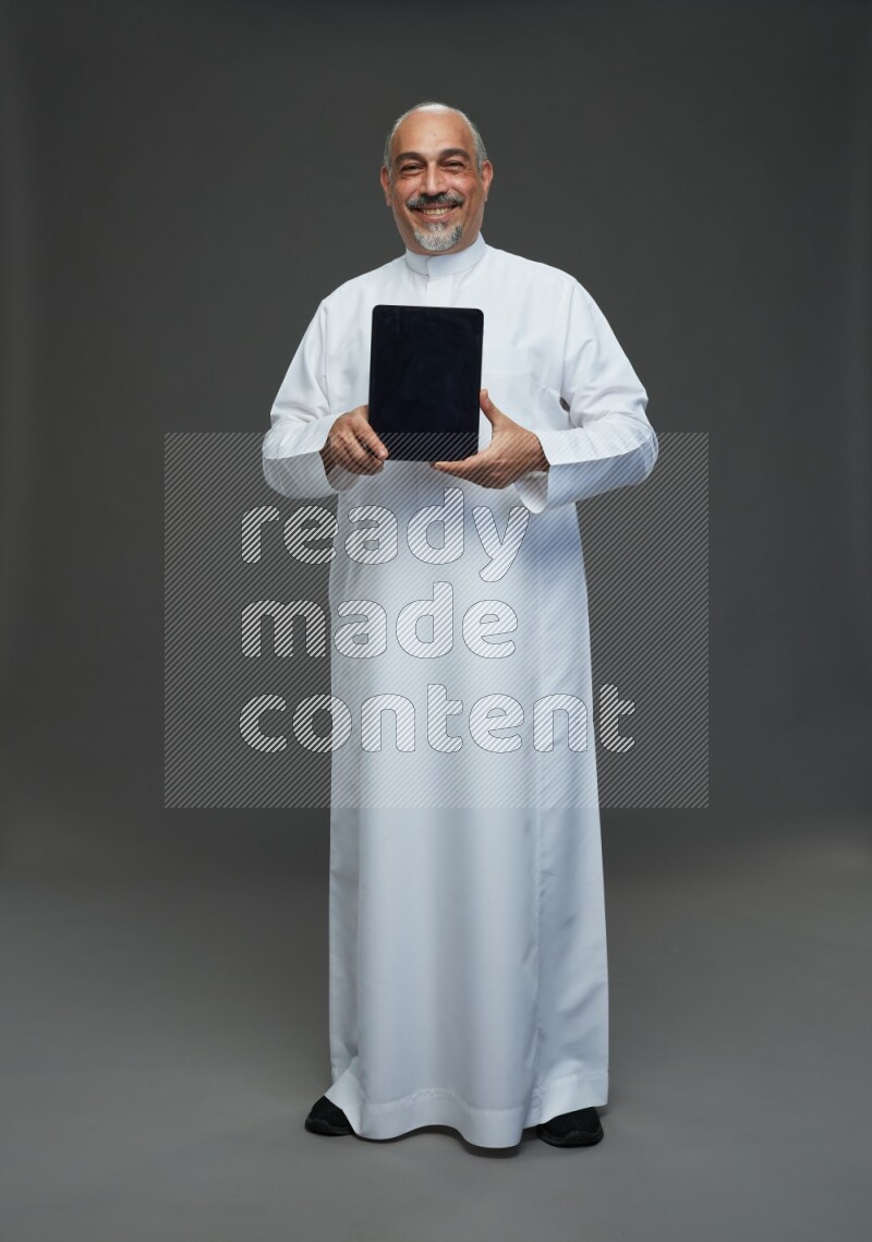 Saudi man without shomag Standing working on tablet on gray background