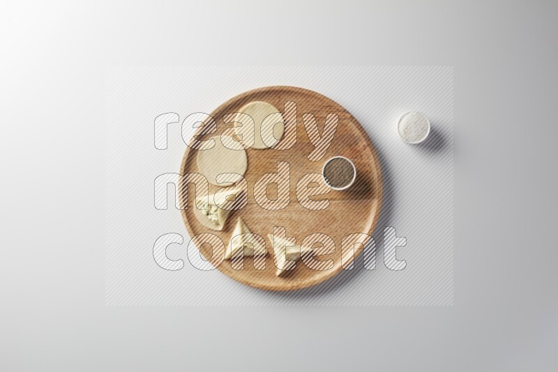 two closed sambosas and one open sambosa filled with cheese while salt, and black pepper aside in a wooden dish on a white background