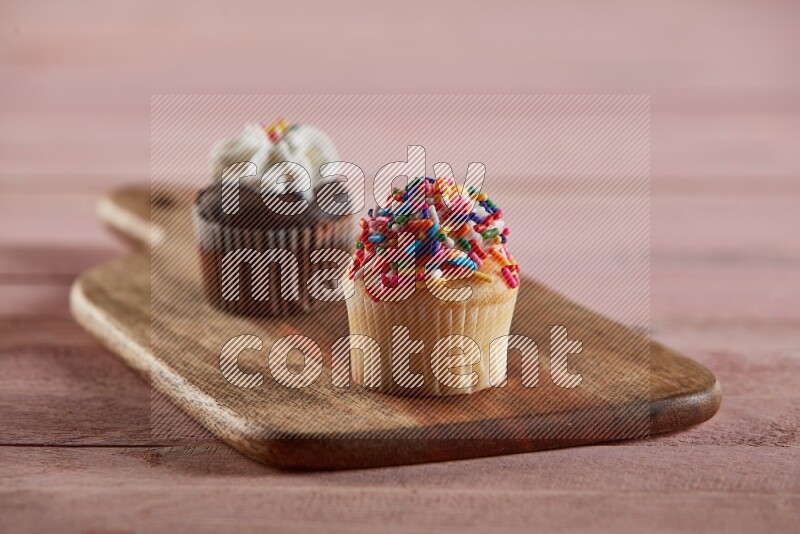 Vanilla mini cupcake topped with sprinkles on a wooden board