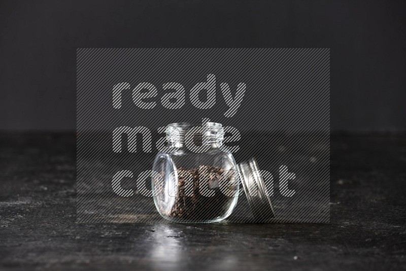 A glass spice jar full of cloves on textured black flooring