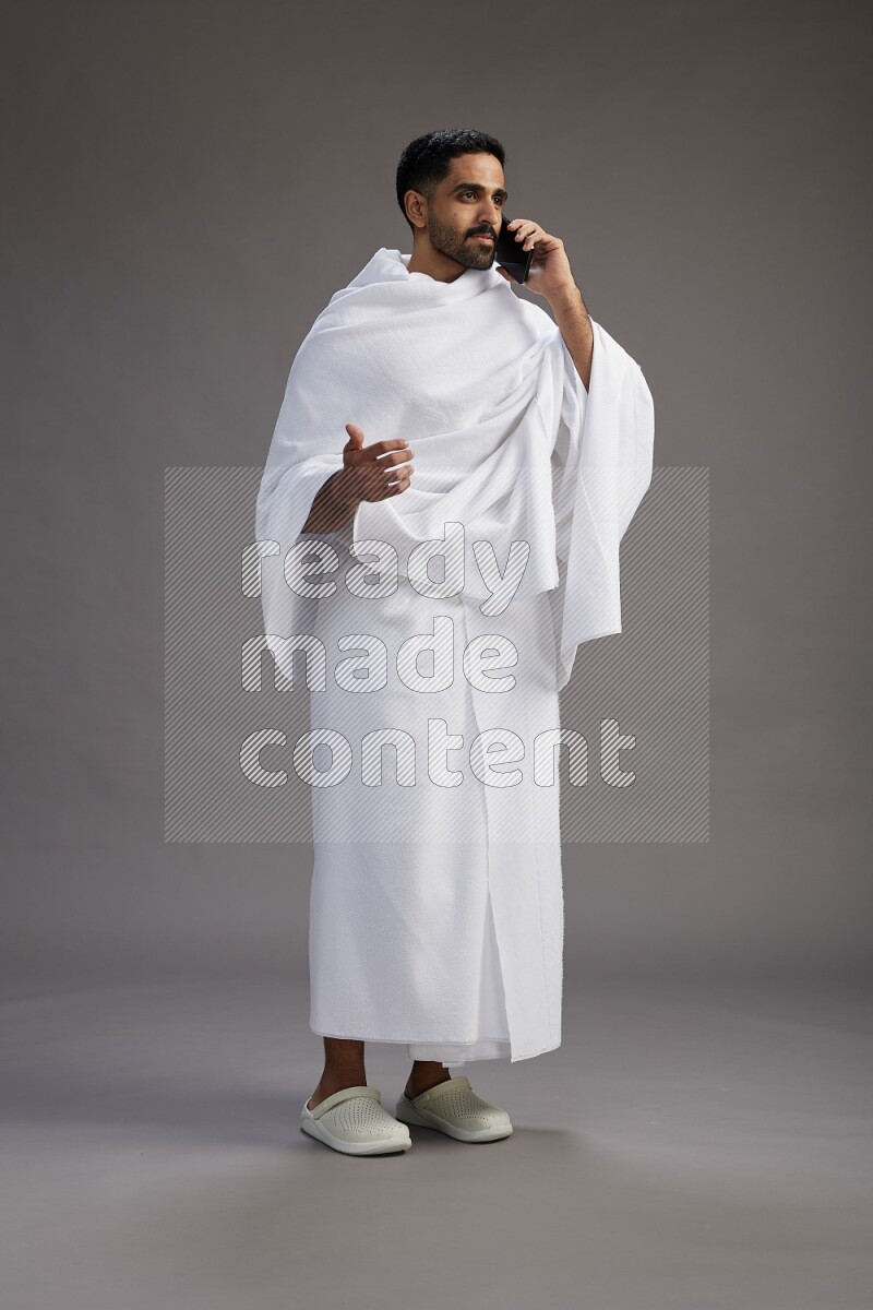 A man wearing Ehram Standing talking on phone on gray background
