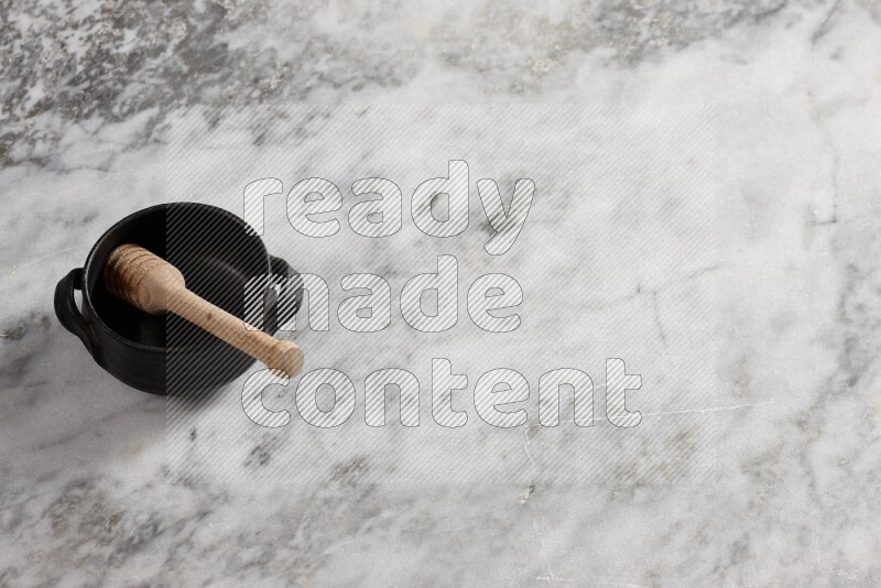 Black pottery bowl with wooden honey dipper in it on grey marble background