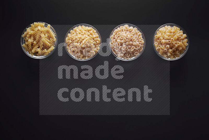 Different pasta types in glass bowls on black background