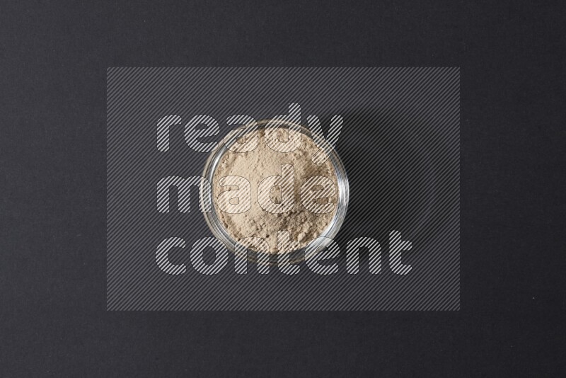 A glass bowl full of garlic powder on a black flooring