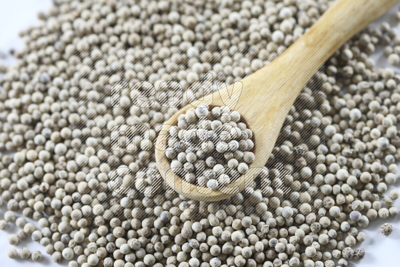 White pepper beads with wooden spoon on white background