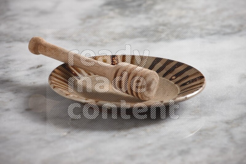 Multicolored pottery plate with wooden honey dipper in it on grey marble background