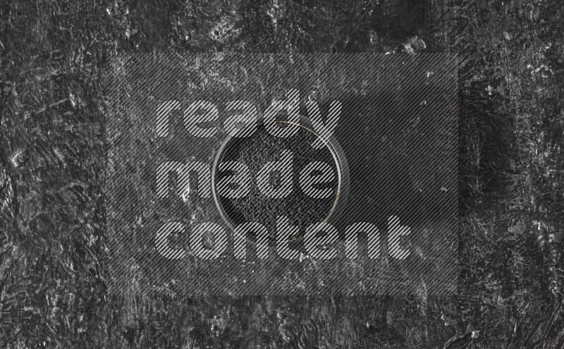 A black pottery bowl full of black seeds on a textured black flooring