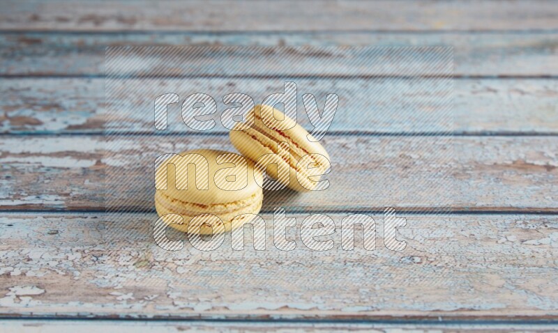 45º Shot of two Yellow Vanilla macarons on a light blue wooden background