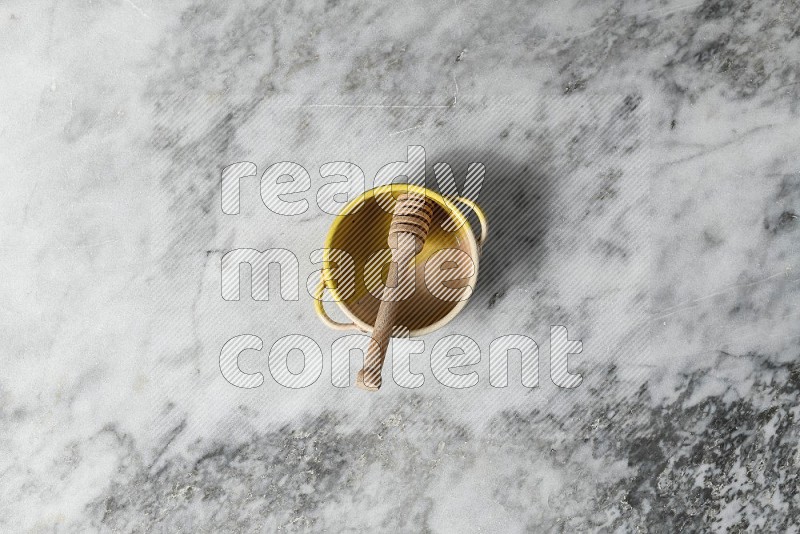 Multicolored Pottery Bowl with wooden honey handle in it, on grey marble flooring, Top View