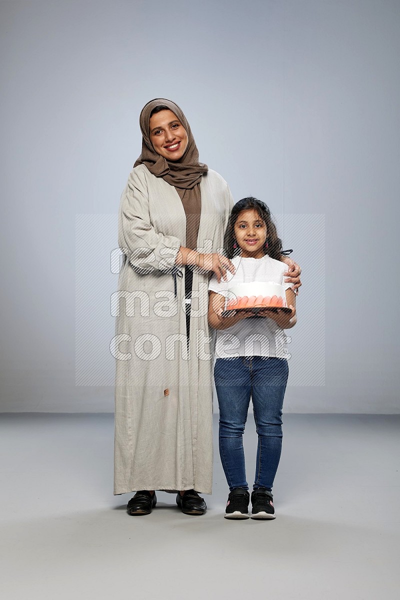 A girl giving a cake to her mother on gray background