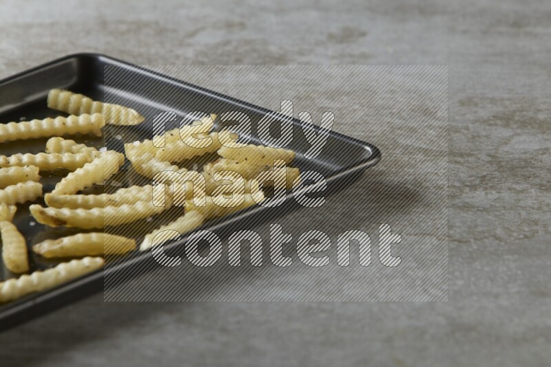 crinkle fries in a black stainless steel rectangle tray on grey textured counter top