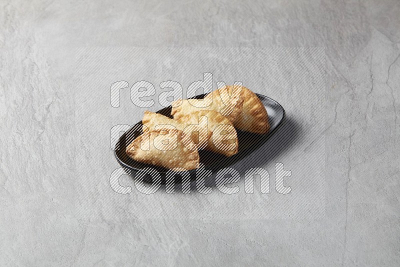 Five fried sambosas in an oval shaped black plate on a gray background
