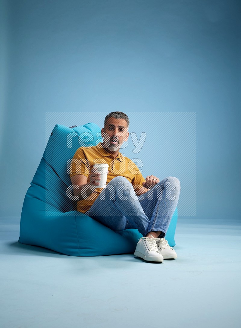 A man sitting on a blue beanbag and drinking coffee