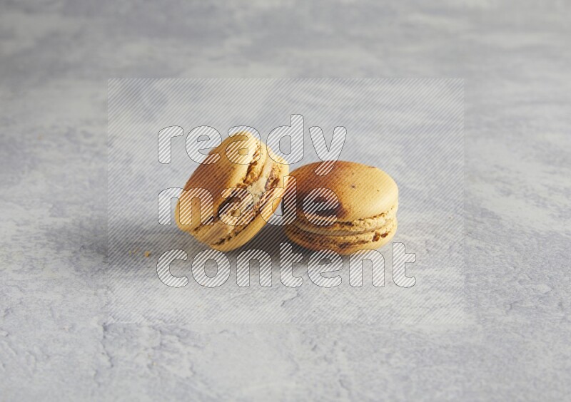 45º Shot of two Yellow Crème Brulée macarons on white  marble background