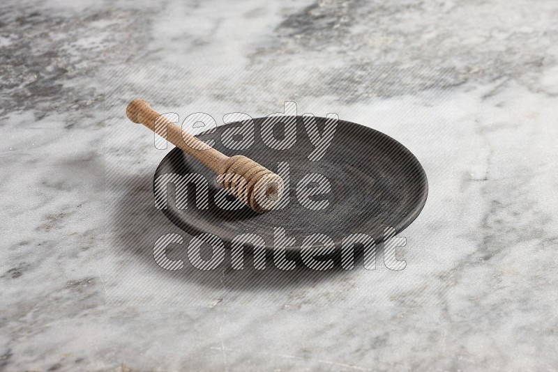 Black Pottery Plate with wooden honey handle in it, on grey marble flooring, 45 degree angle