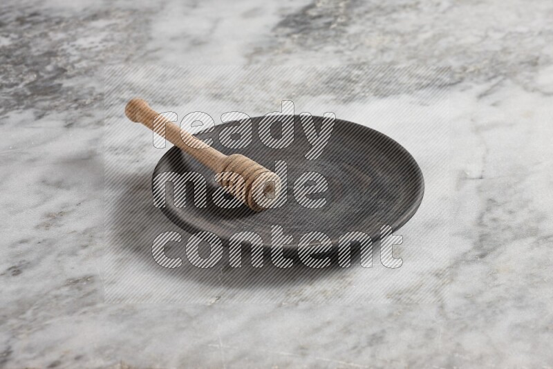 Black pottery plate with wooden honey dipper in it on grey marble background