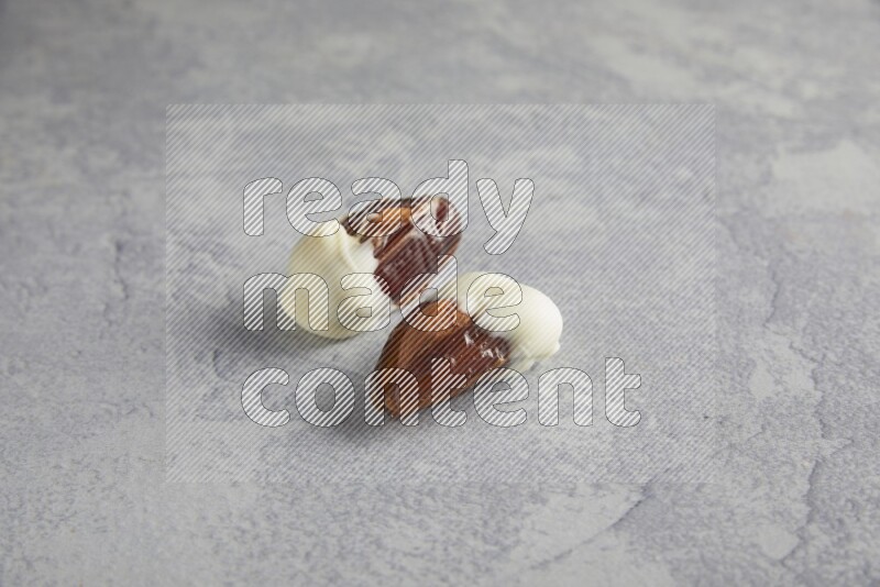two almonds stuffed dates covered with white chololate on a light grey background