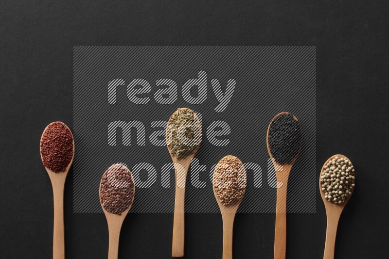 الفلفل الأسود وحبوب الخردل وحبة البركة وحب الرشاد والكمون و حبوب الكتان في معالق خشبية علي خلفية سوداء