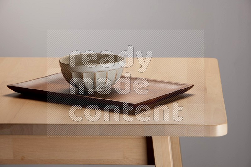 off white bowl placed on a rectangular wooden tray on the edge of wooden table