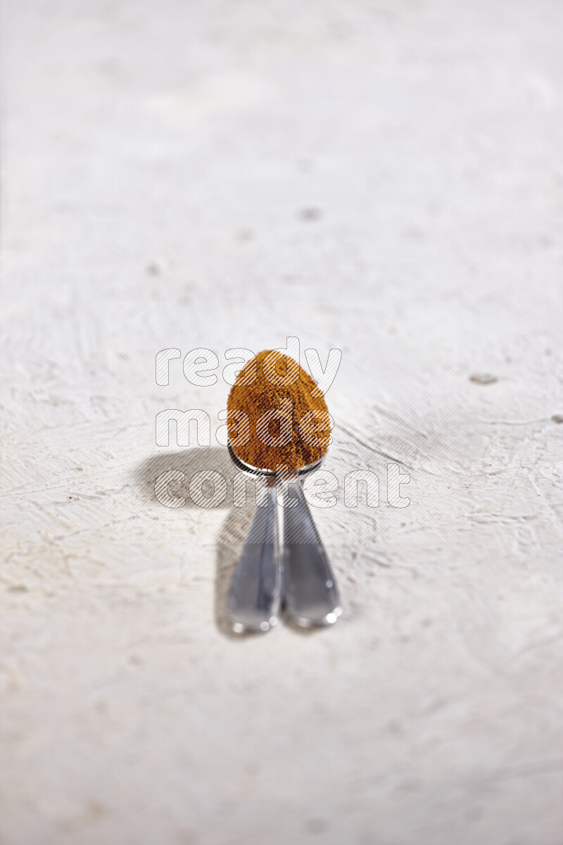 Two metal spoons full of ground paprika powder on white background