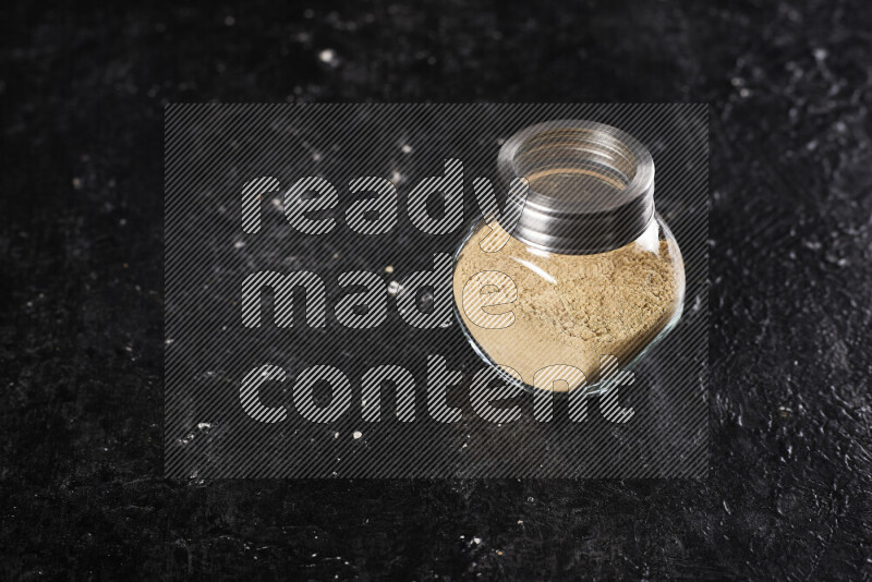 A glass jar full of ground ginger powder on black background