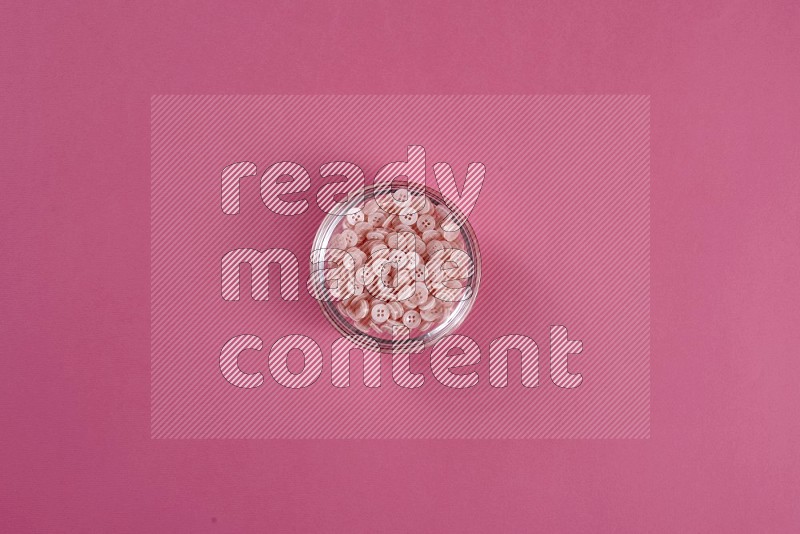A glass bowl full of pink buttons on pink background