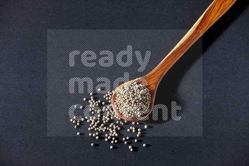 A wooden ladle full of white pepper beads on black flooring