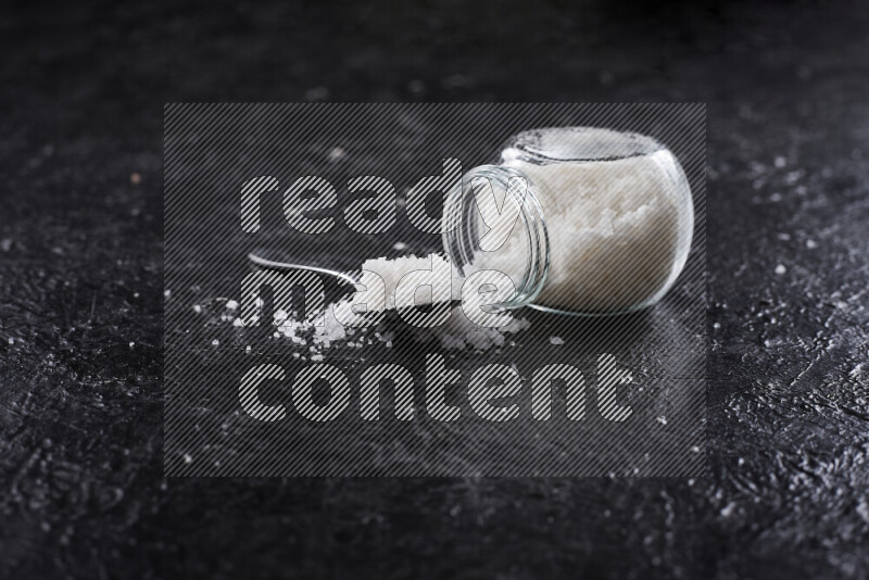 A glass jar full of coarse sea salt crystals on black background